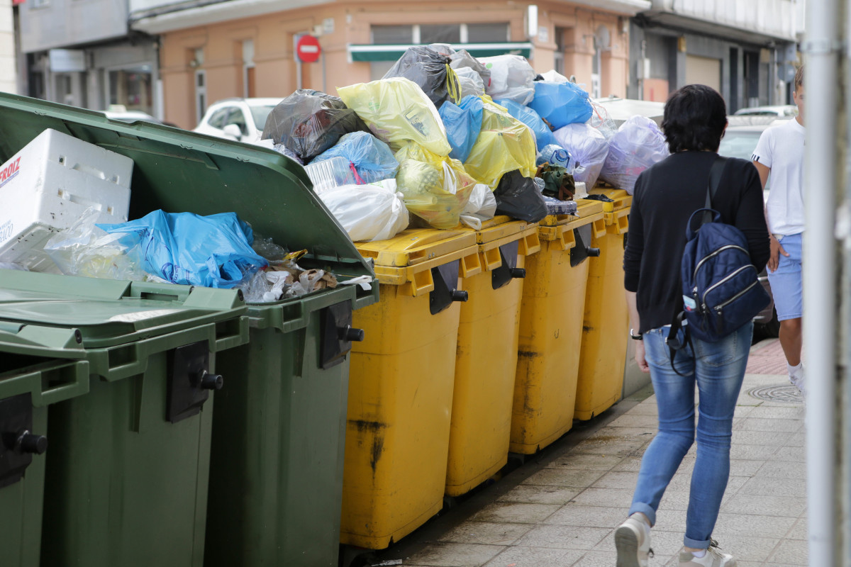 Una mujer camina al lado de contenedores de basura desbordados durante la cuarta semana de la huelga en la recogida de basura de Vilalba, a 11 de septiembre de 2023, en Vilalba, Lugo, Galicia (España